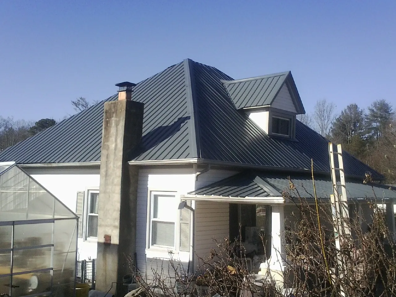 Dark blue standing seam metal roof on a white farmhouse with dormer — Slate & Tile Roof Repair by Roofing Brothers in Sylva