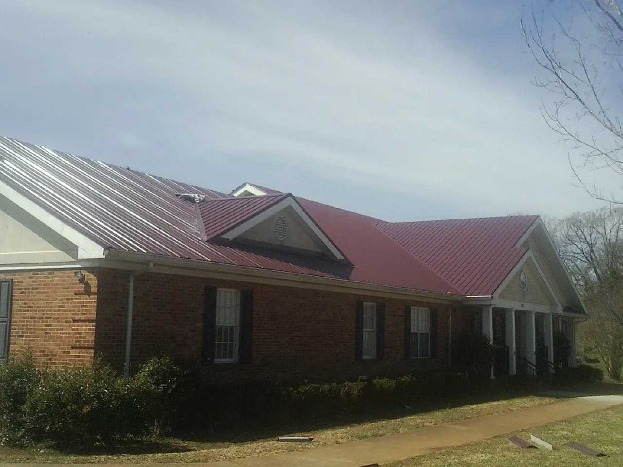 Red metal roof with gabled entries on a long brick building, from a Hail Damage Roof Repair job in Sylva