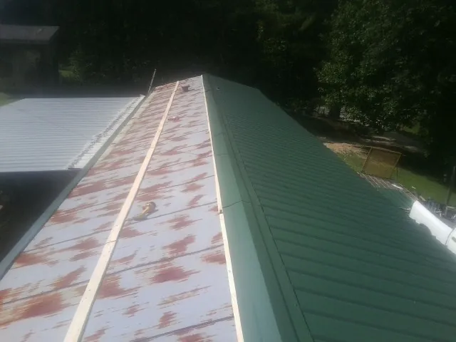 Old rusted panels beside newly installed green metal roofing — Wind Damage Roof Repair by Roofing Brothers in Sylva