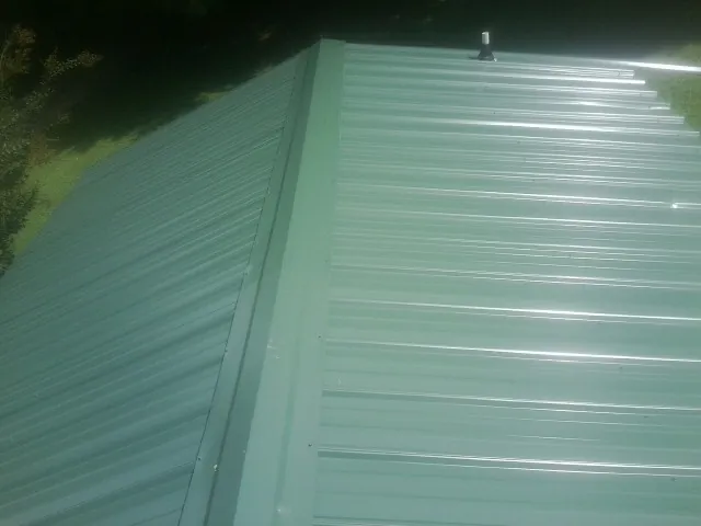 New green metal panels meeting at the ridge of a roof — Flat Roof Repair work by our crew in Sylva