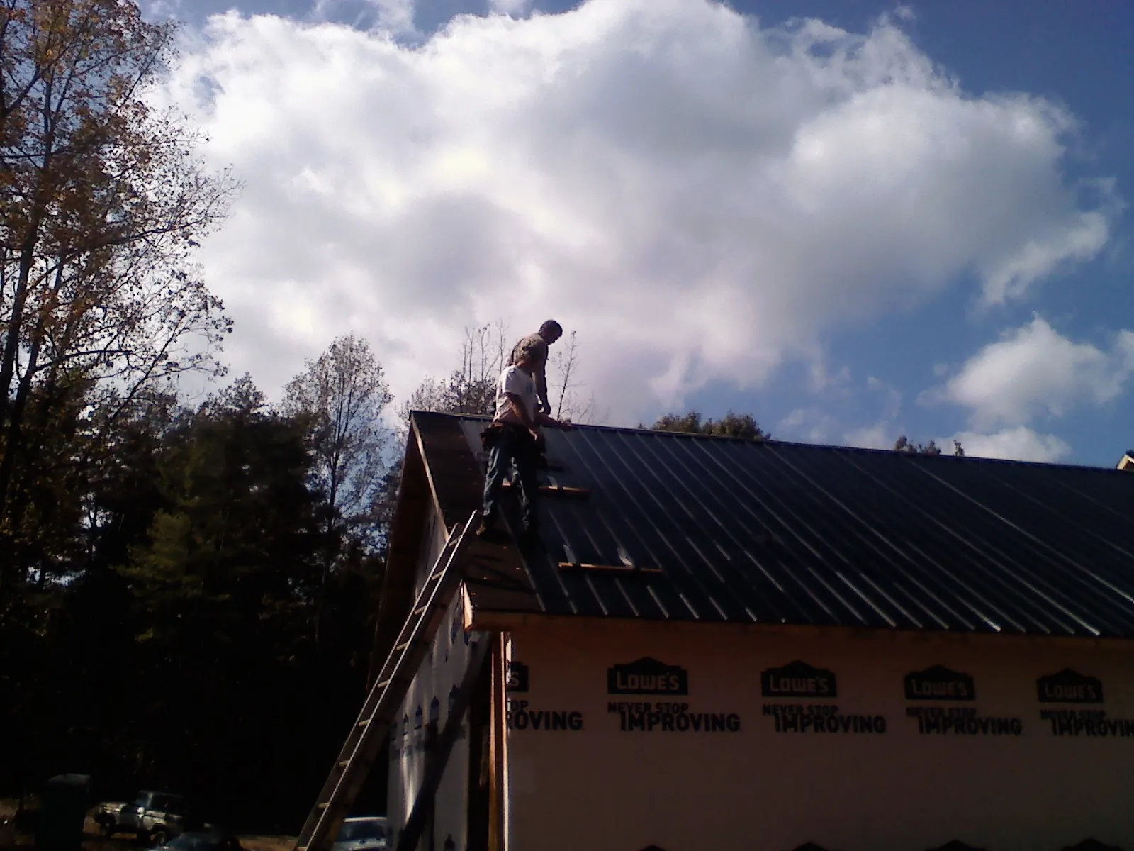 Roofer fastening dark metal panels high against a cloudy sky, from a Roof Inspection job in Sylva