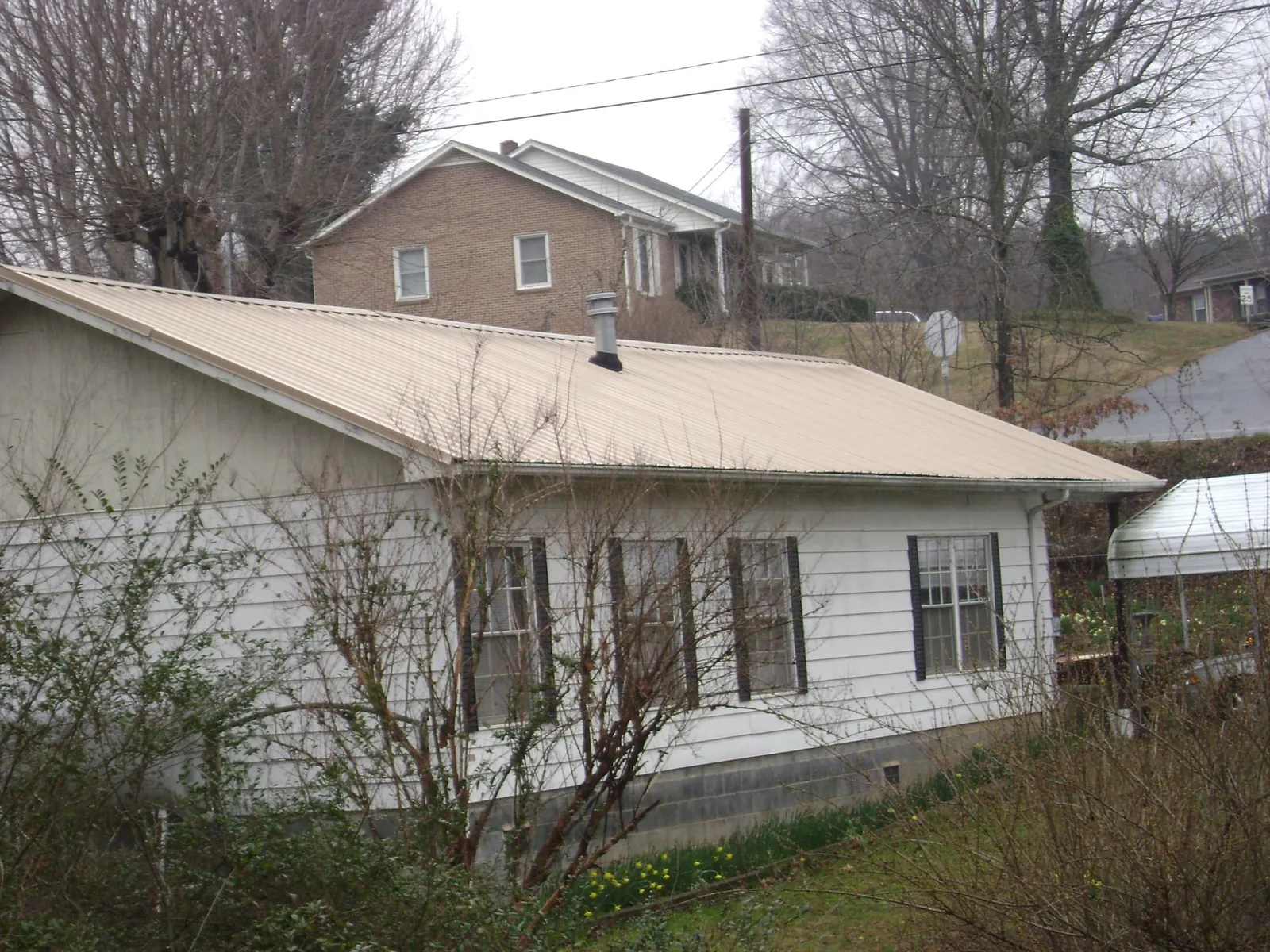 Tan metal roof on a white sided house set into a hillside — Commercial Roofing by Roofing Brothers in Sylva