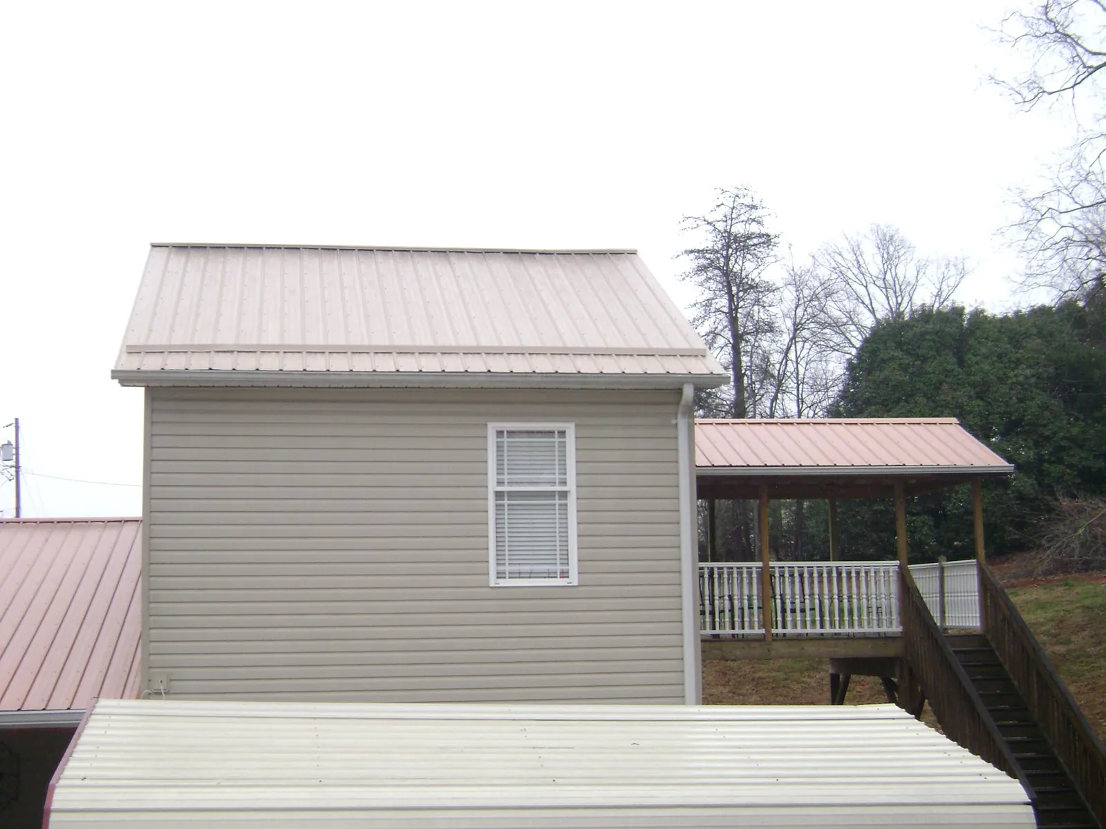 Tan metal roofs on a two story addition and attached porch, from a Roof Replacement job in Sylva
